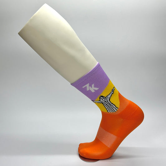 Calcetas personalizadas deportivas para carrera 7K. Calceta en color morado, amarillo y naranja con el icono de un cristo con los brazos abiertos en blanco y negro. 