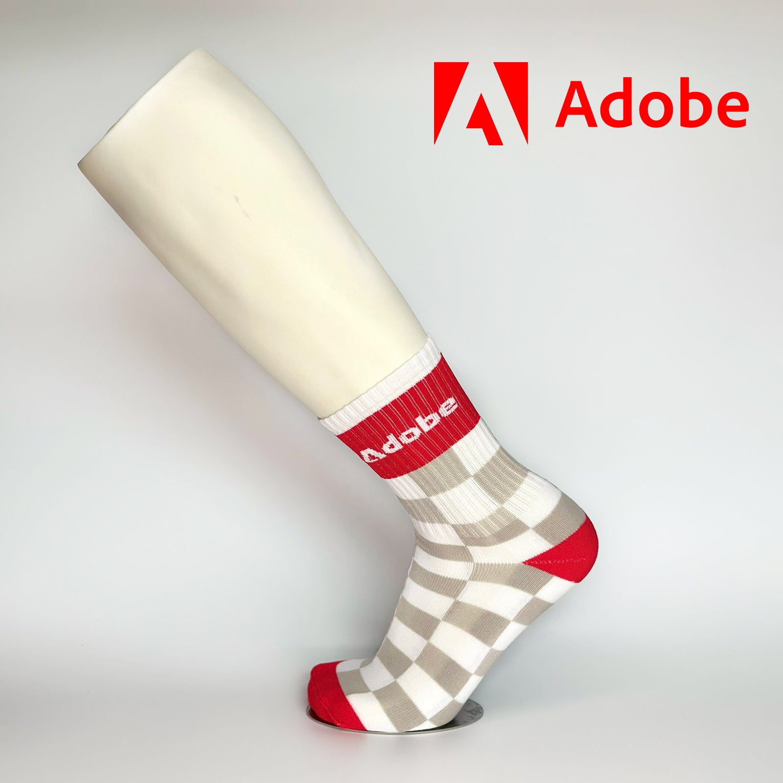 Calcetas personalizadas deportivas con patrón de cuadrados blanco con gris y una franja roja donde se posiciona el logo de ADOBE. ADOBE las utilizó como regalo navideño a sus empleados. 