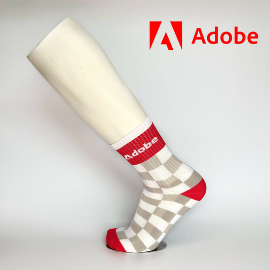 Calcetas personalizadas deportivas con patrón de cuadrados blanco con gris y una franja roja donde se posiciona el logo de ADOBE. ADOBE las utilizó como regalo navideño a sus empleados. 