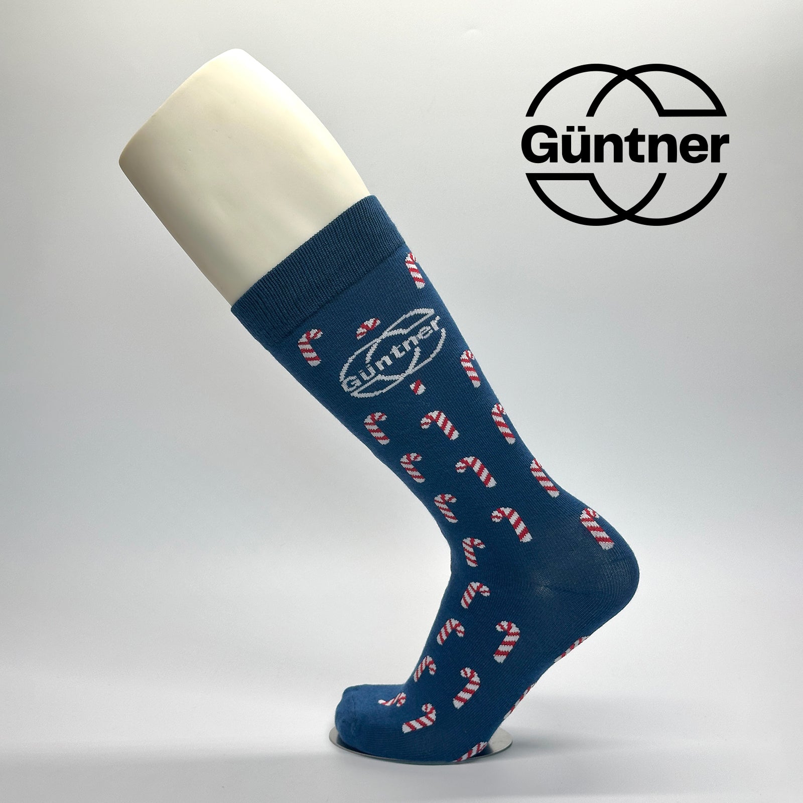 Calcetas de vestir personalizadas para la empresa gunter como regalo navideño. El diseño es de base azul y trae un patrón de caramelos en color blanco con rojo y el logo de GUNTER en la parte lateral centrado. 