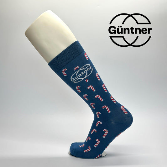 Calcetas de vestir personalizadas para la empresa gunter como regalo navideño. El diseño es de base azul y trae un patrón de caramelos en color blanco con rojo y el logo de GUNTER en la parte lateral centrado. 