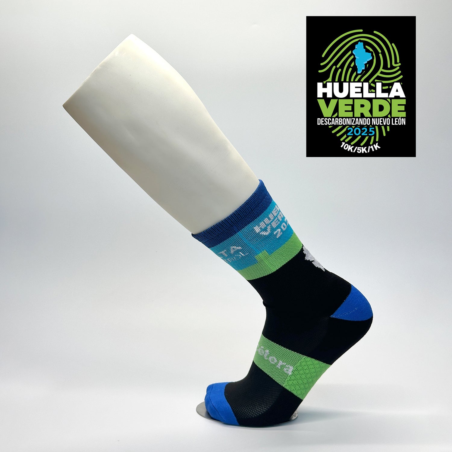 Calcetas personalizadas deportivas con diseño en colores negro, verde, azul y blanco. La calceta tiene el logo de la carrera Huella Verde 2025 así como dos logos de empresas patrocinadoras. La calceta fue parte del kit de la carrera. 