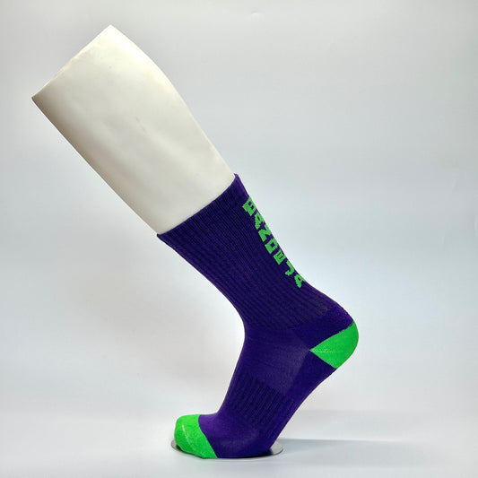 Calcetas personalizadas deportivas color morado con detalles en verde fosfo y la frase "Bandeja" en la parte trasera. Las calcetas las compraron para venderlas en unas canchas de paddel y son temáticas de paddel. 