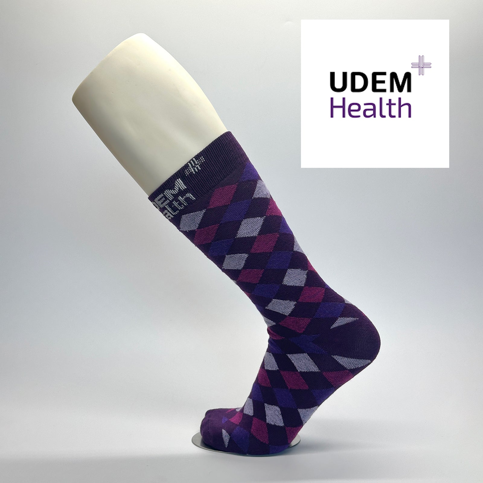 Calcetas personalizadas de vestir moradas con rombos en diferentes tonos de morado y el logo de UDEM HEATLH. 