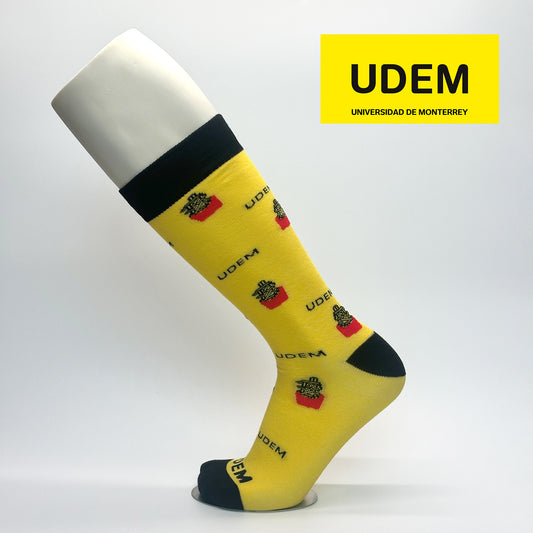 Calcetas personalizadas de vestir amarillas con icono emblematico del campus UDEM así como el logo de la empresa Universidad. La calceta se vende en la tienda oficial de la universidad.