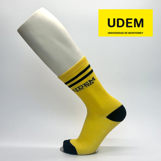 Calcetas personalizadas de vestir estilo retro color amarillas con icono de la UDEM y una frase "EST.1969". La calceta se vende en la tienda oficial de la universidad.