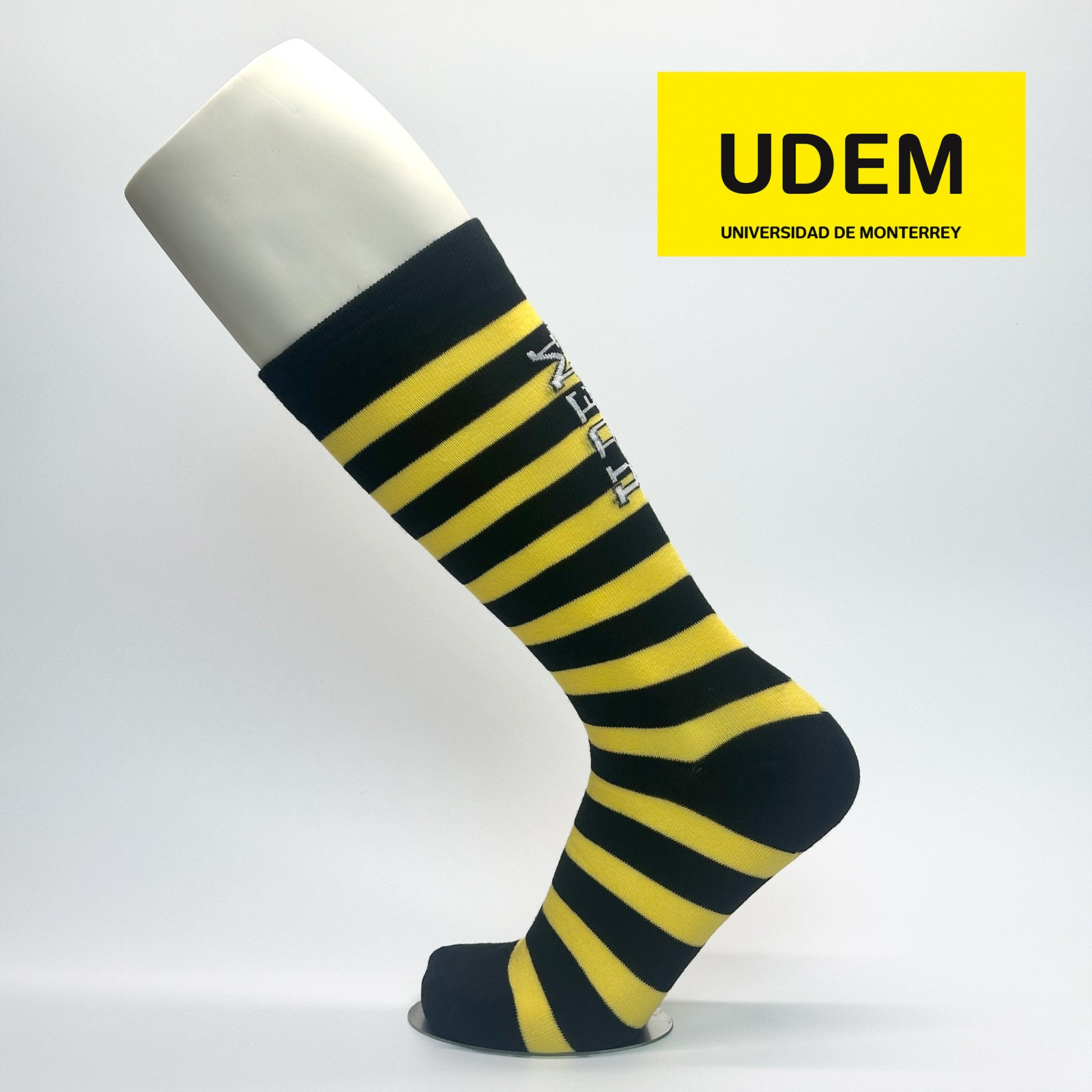 Calcetas personalizadas de vestir con rayas negro y amarillo y logo de la UDEM. La calceta se vende en la tienda oficial de la universidad.