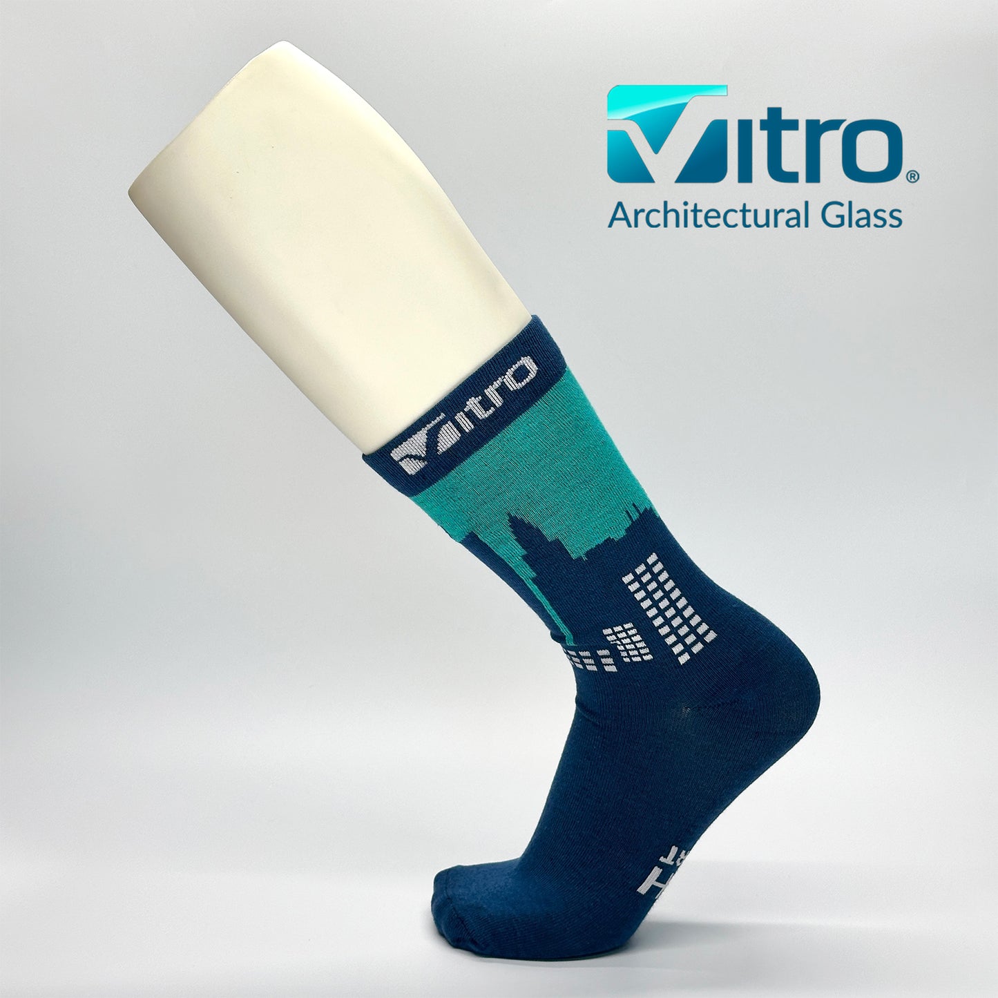 Calcetas personalizadas de vestir con ilustración de edificios con la luz prendida en el atardecer. Además, la calceta tiene el logo de VITRO quien los uso como regalo a sus clientes. 